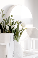 Rounded marble stone bookends styled with tulips and books on a white console for elegant minimalist home decor.