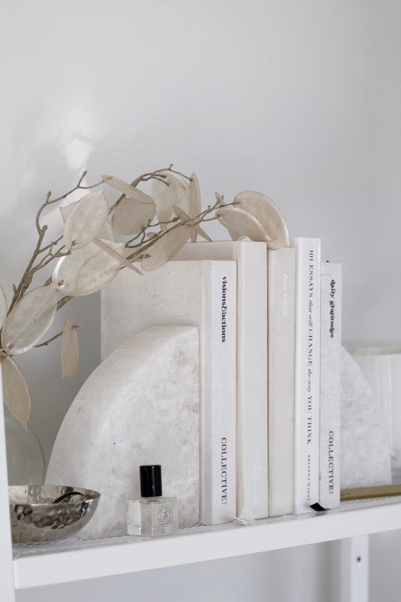 Rounded marble stone bookends by Papier HQ holding white books on a minimalist shelf with neutral styling.