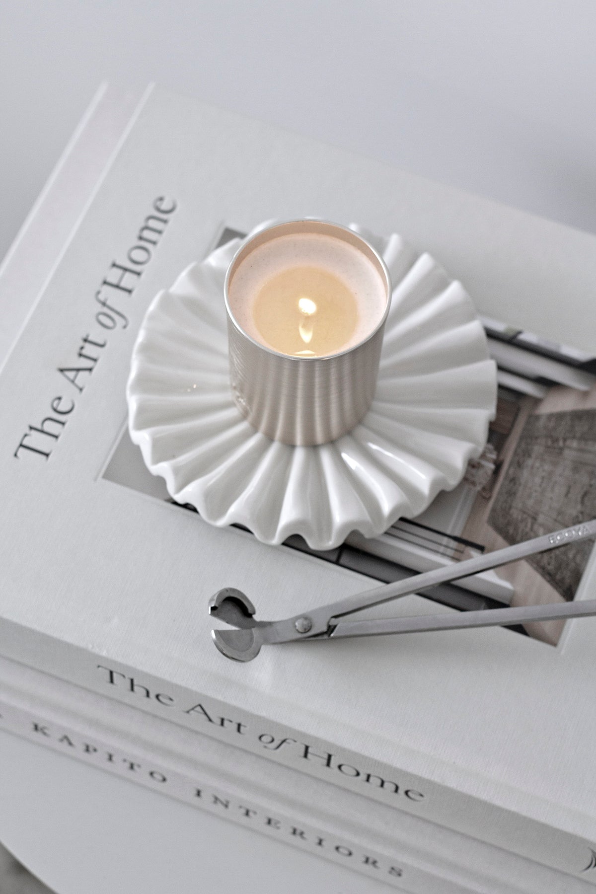 White ruffle tray holding a lit candle and wick trimmer on a stack of design books