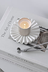 Small white ceramic display tray with ruffled edges styled with a lit candle and wick trimmer on a stack of interior design books.
