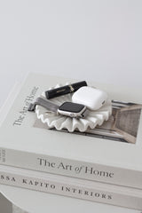Glossy white ruffle ceramic display tray used as a catchall for jewellery and essentials; styled on coffee table book