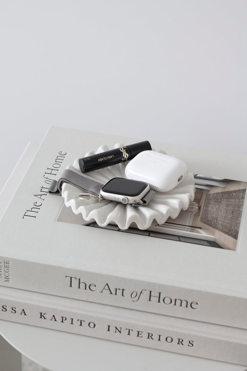 Glossy white ruffle ceramic display tray used as a catchall for jewellery and essentials; styled on coffee table book