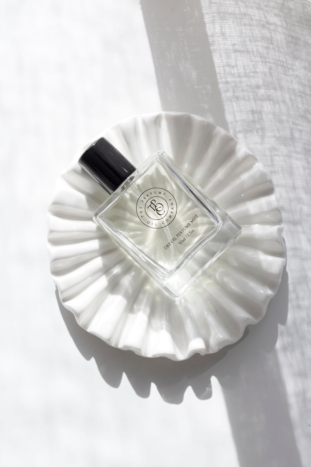 Perfume bottle on the white ruffle ceramic tray, seen from above