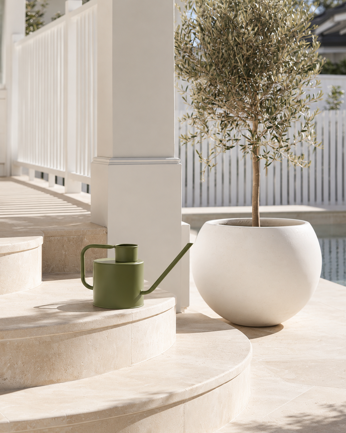 Merlino watering can in avocado on a curved stone step beside a white planter with an olive tree