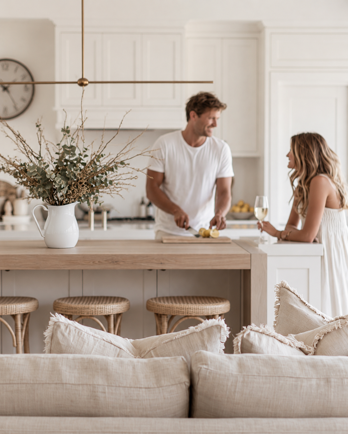 White enamel water jug of dried foliage on a timber kitchen island in a bright white kitchen