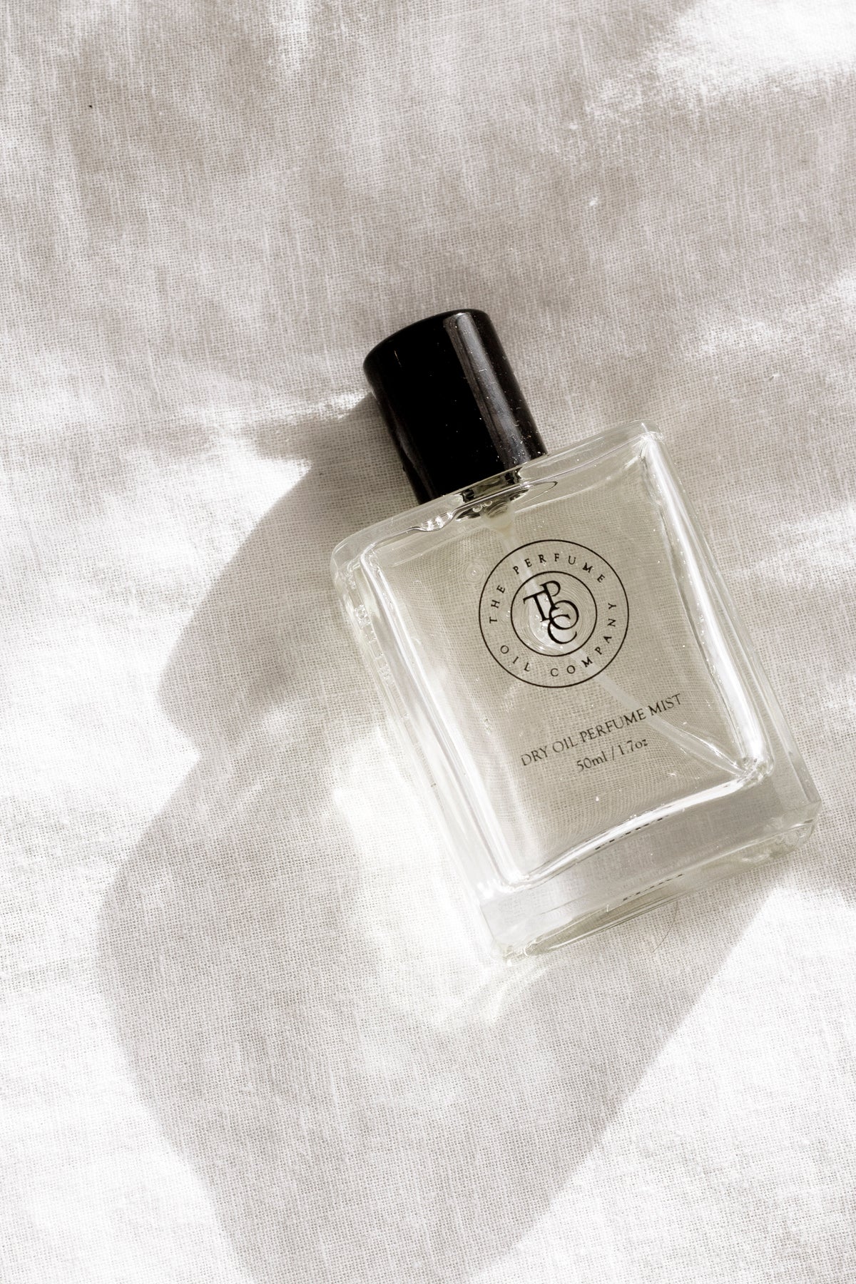 Perfume oil bottle resting on sunlit white linen with soft shadows