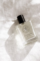 Minimalist fragrance bottle on sunlit linen fabric with soft shadows, clean neutral aesthetic.
