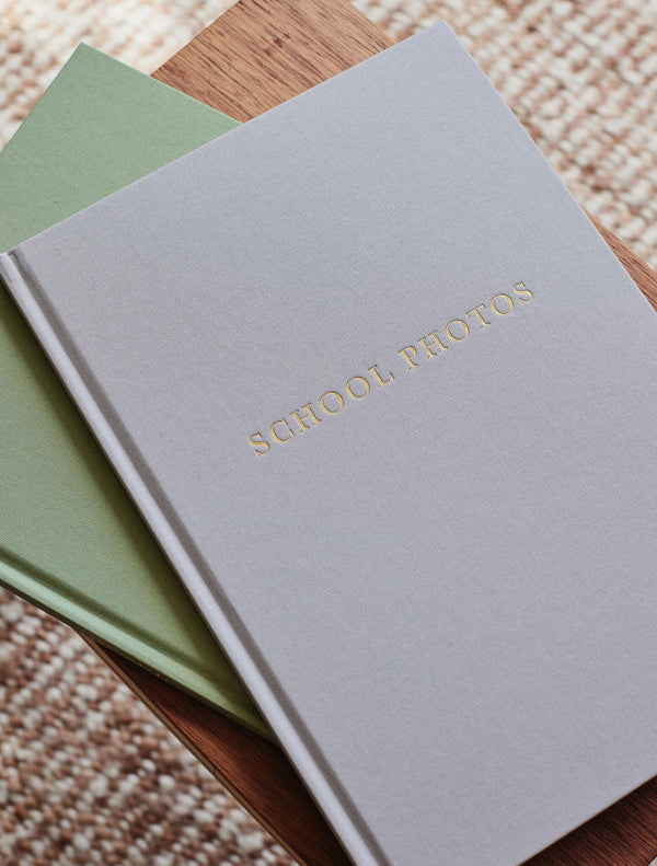 Grey linen School Photos journal stacked on a sage journal on a woven rug