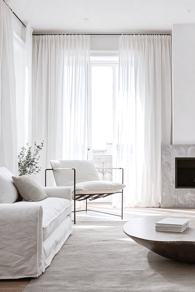 Bright minimalist living room with sheer white curtains, textured neutral rug, a low round stone coffee table, and the Scout Lounge Chair in white leather and black iron frame.