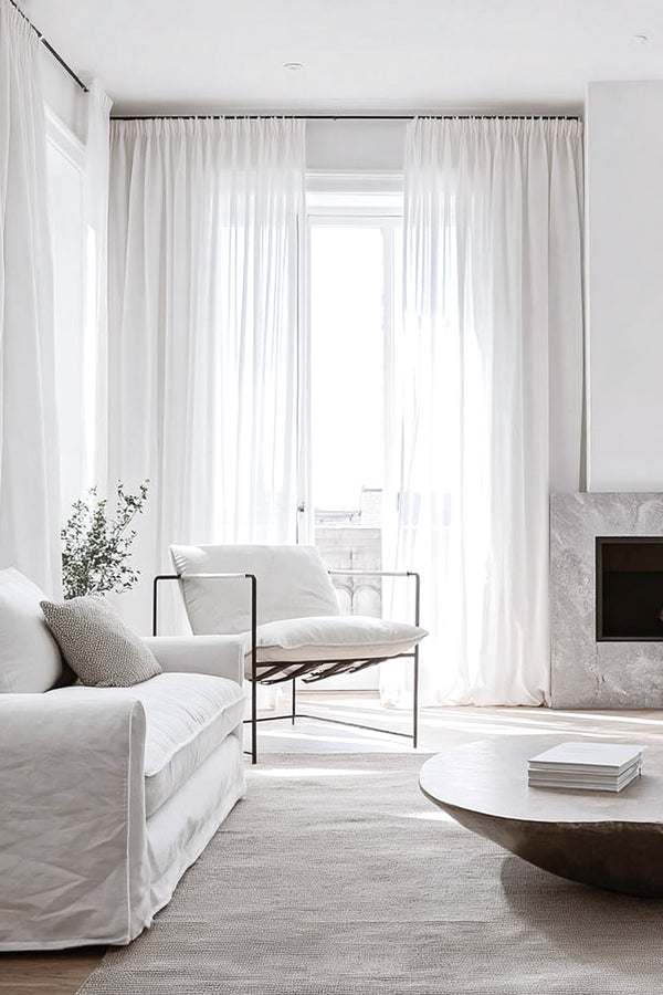 A modern lounge chair with soft vintage white leather cushions and a black metal frame, styled in a bright living room with sheer curtains and a textured neutral rug.