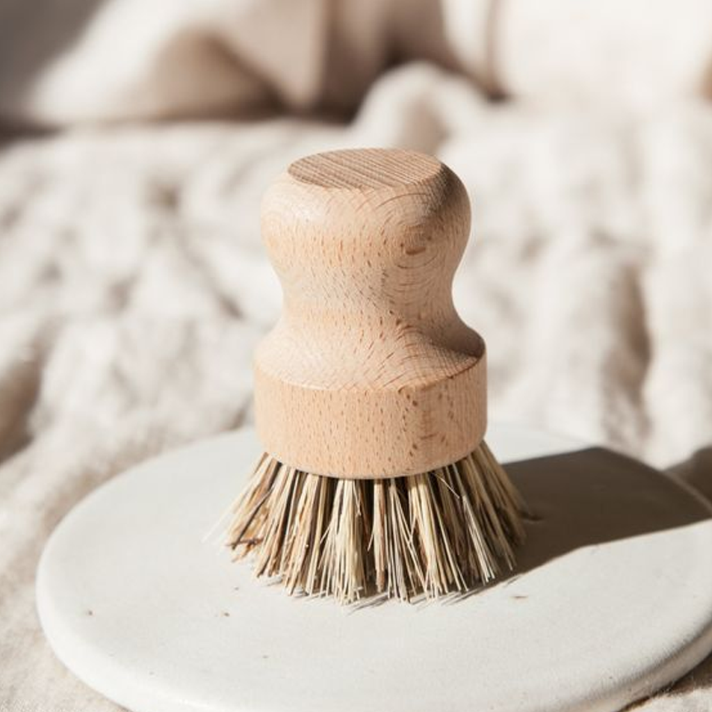 Pot brush resting on a white plate on a knitted throw