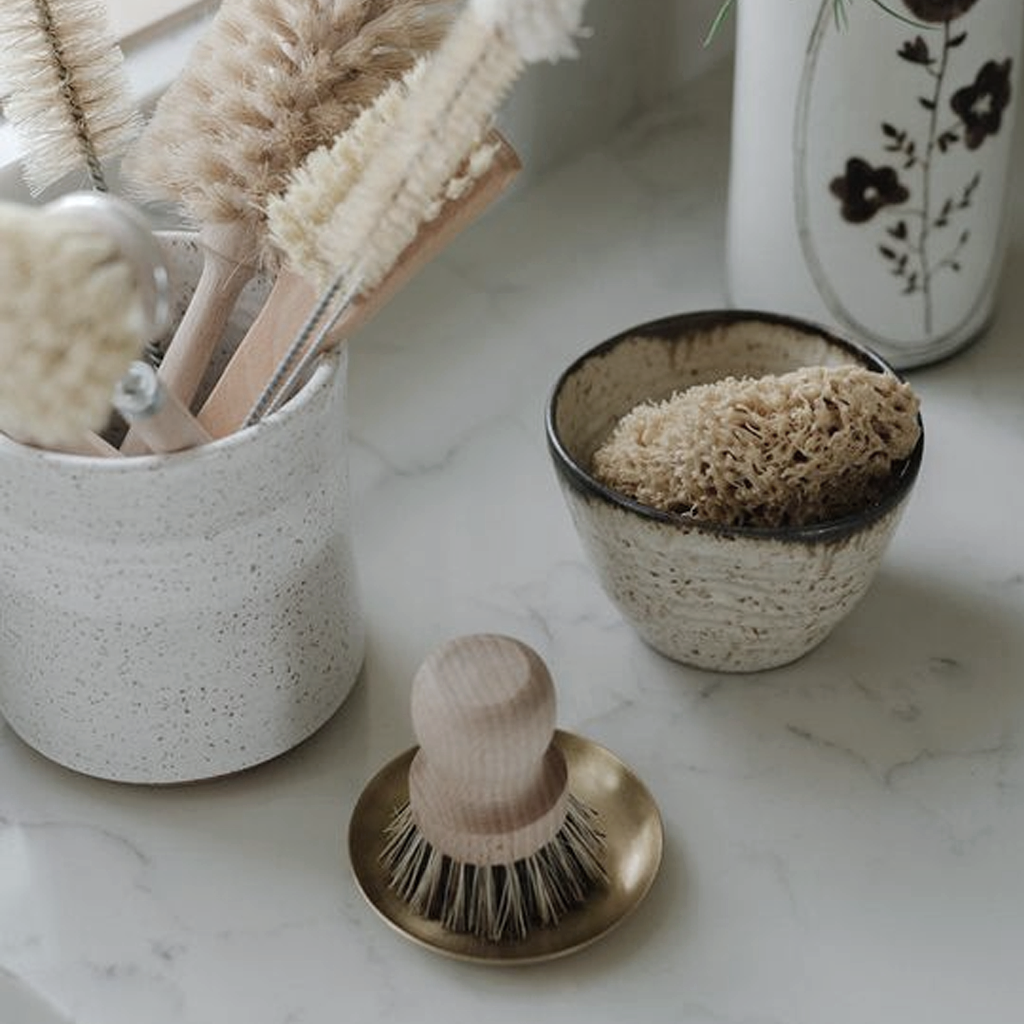 Pot brush beside a white cup of brushes and a ceramic dish