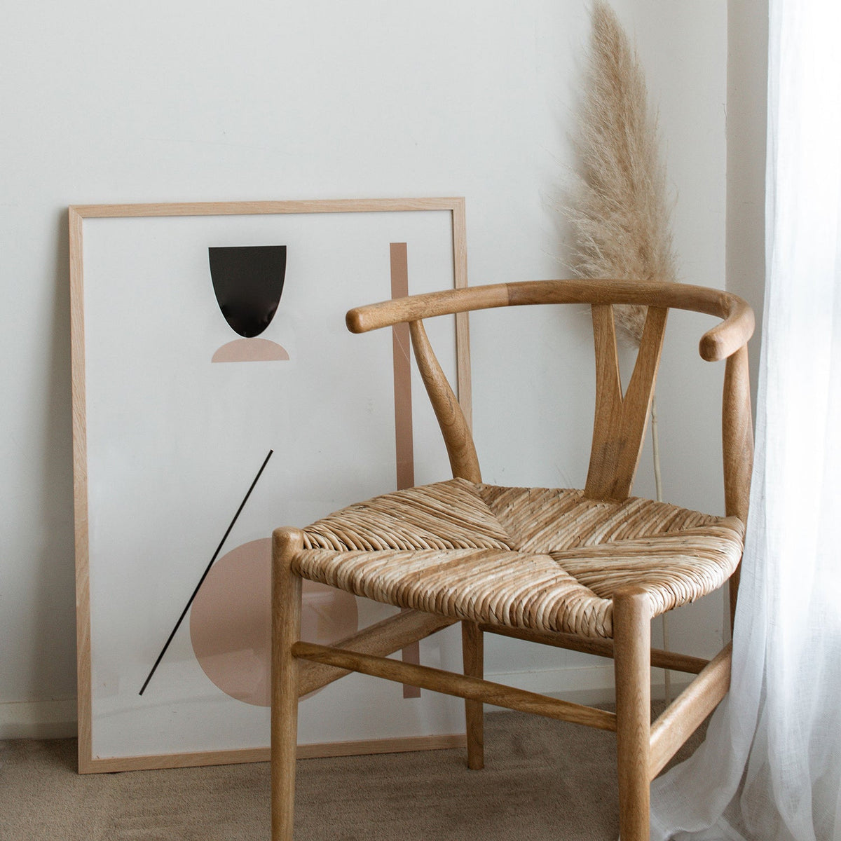 Shape Abstract print in sand in a natural frame beside a woven wishbone chair