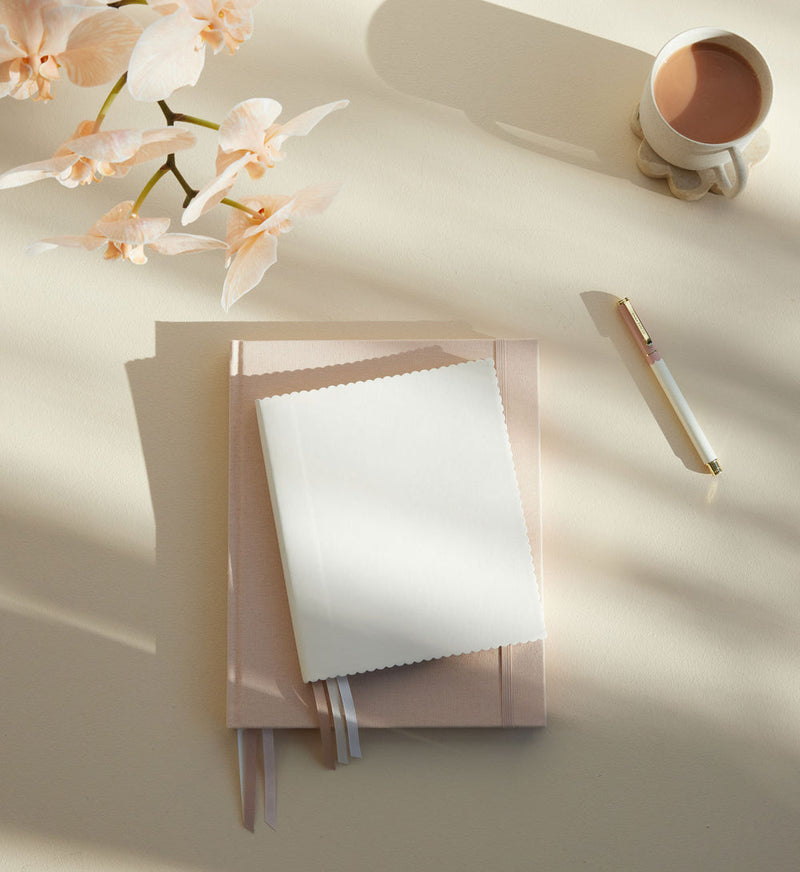 Cream scallop edge journal styled on a neutral desk with orchid, coffee cup and pen in warm morning light