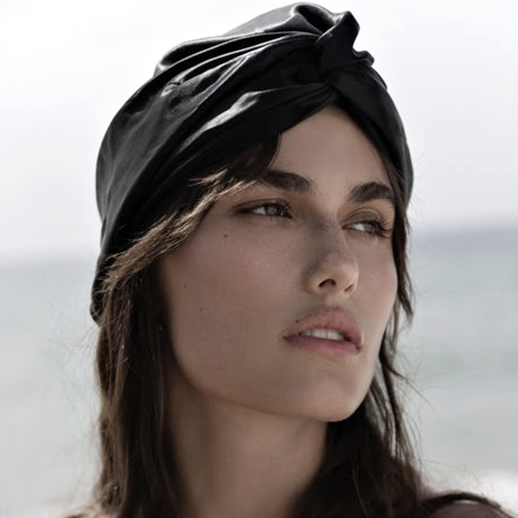 Woman wearing the black mulberry silk sleep bonnet outdoors with the sea behind her