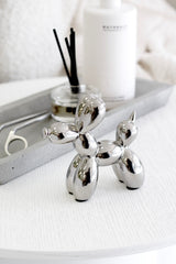 Silver balloon dog sculpture styled on white table beside diffuser and tray