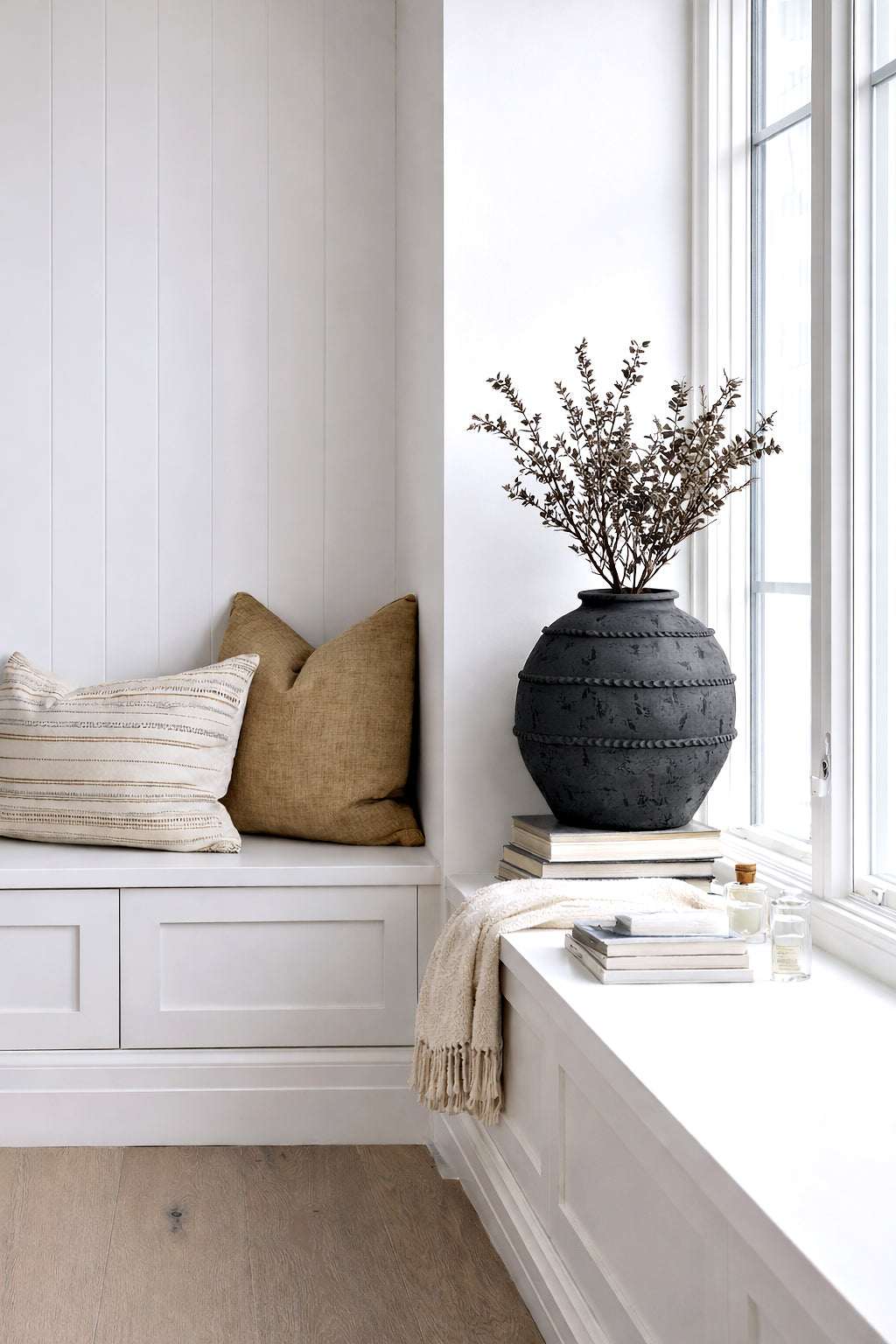 Black Sirocco vase of fine dried blossom on a window seat beside linen cushions