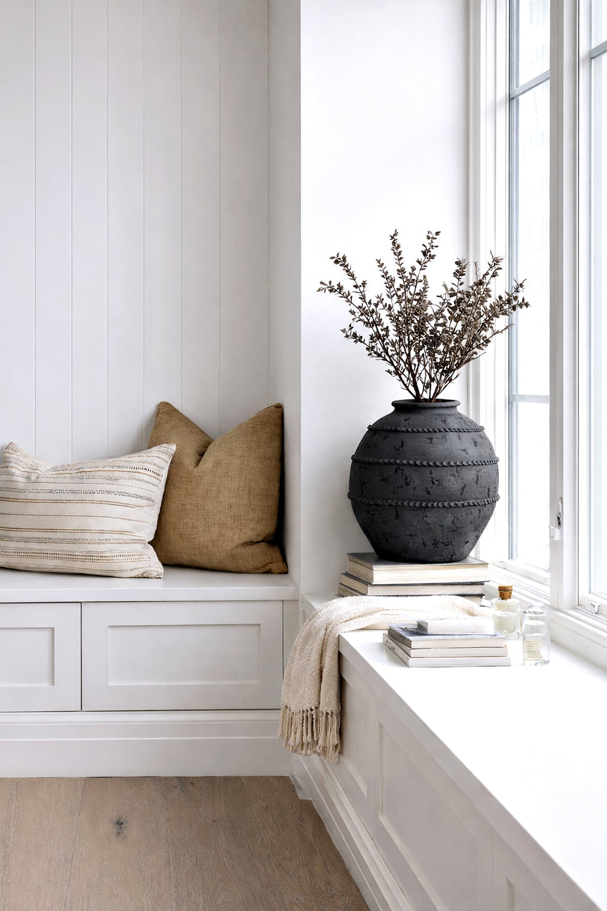 Black Sirocco vase of fine dried blossom on a window seat beside linen cushions