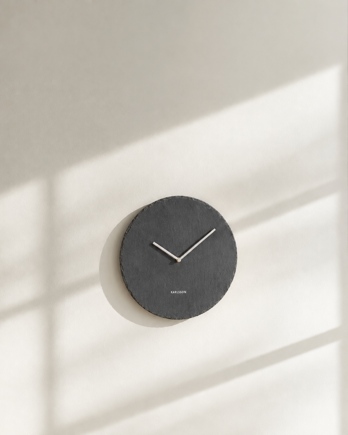 Karlsson slate wall clock in charcoal hung on a warm white wall in dappled sunlight