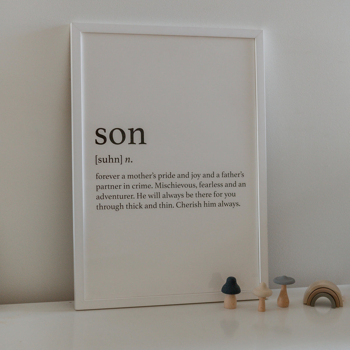 Son print in a white frame leaning on a shelf beside small wooden toys