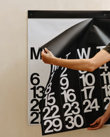 Hands holding the oversized Stendig wall calendar against a beige wall