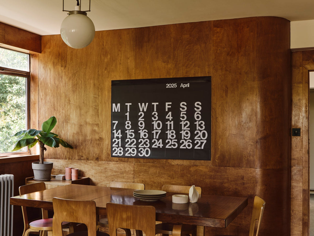 Stendig Calendar by Massimo Vignelli on a wood panelled wall in a warm interior
