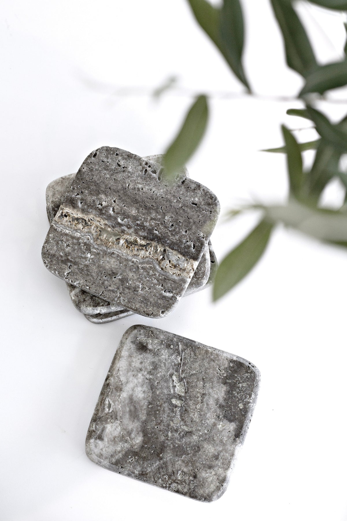 Set of four dark marble travertine stone coasters in natural finish; square design with earthy texture for modern styling.