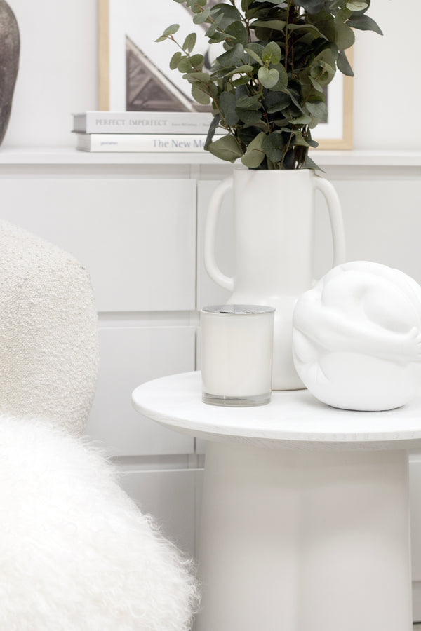 Strato white side table styled with candle, sculptural vase, and greenery beside a boucle armchair