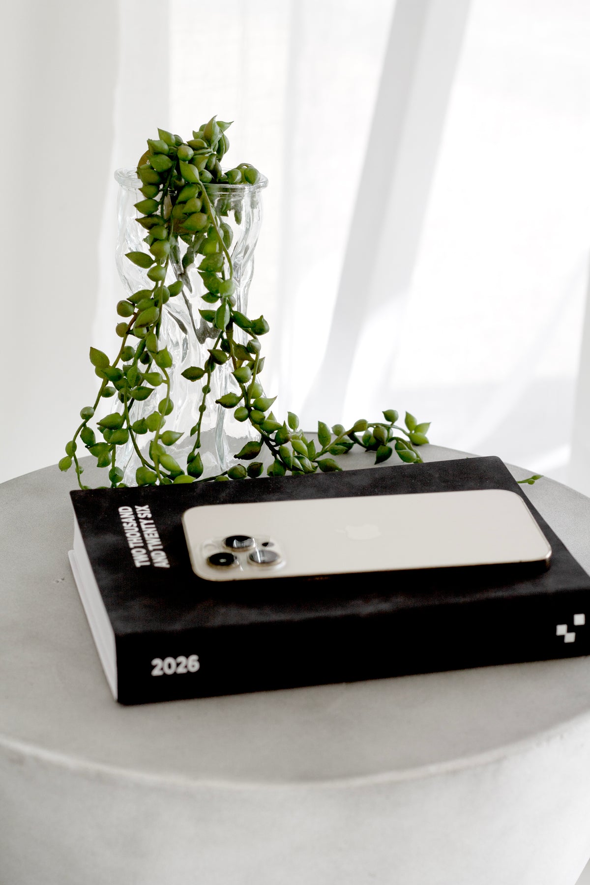 Faux string of tears spilling from a ripple glass vase beside a black diary and phone on a concrete side table