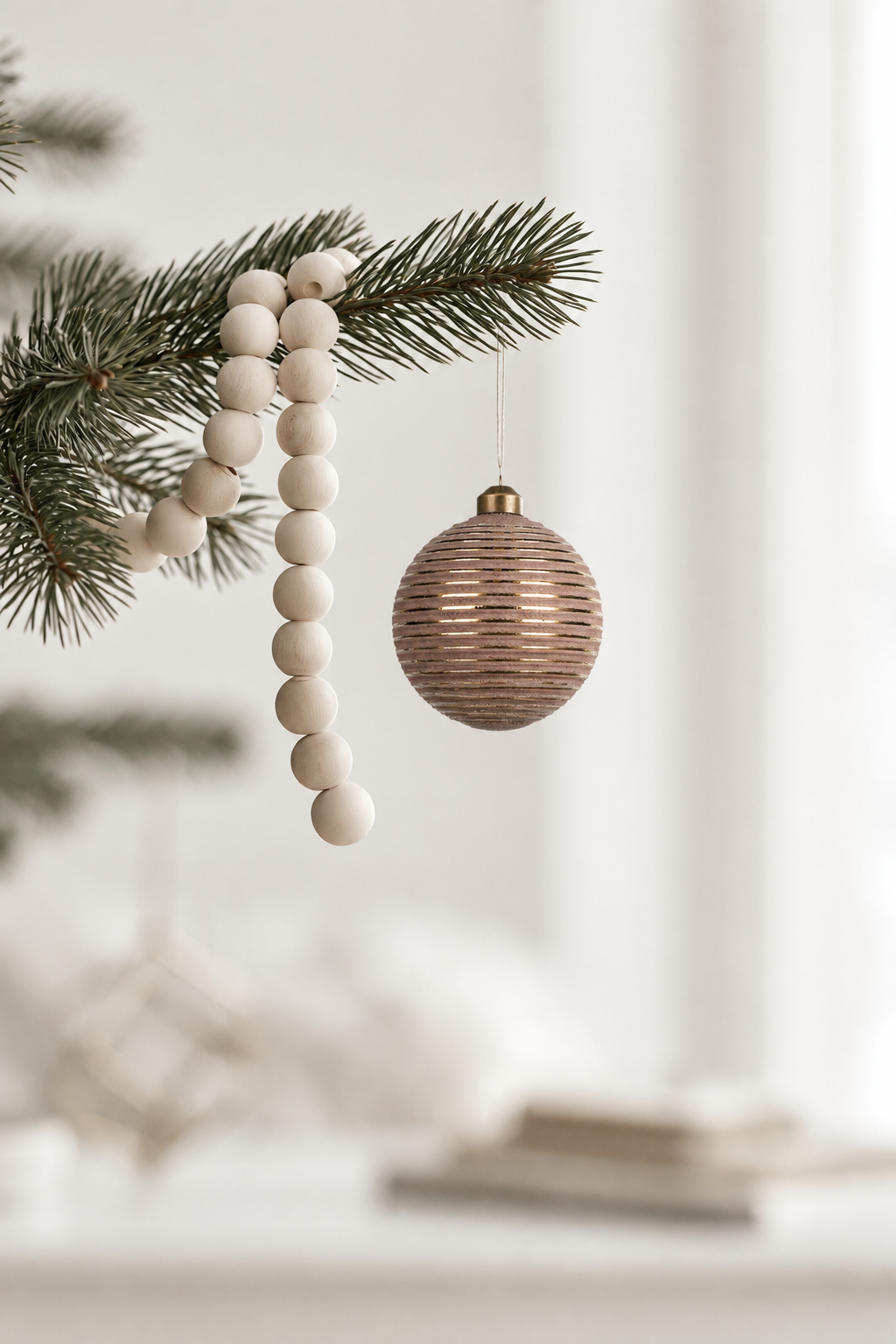 Stripe Pattern Glass Bauble in brown and gold 8cm hanging from a pine branch beside a wooden bead garland