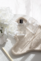 Travertine curved tray with clear perfume bottles and glasses in soft sunlight; neutral “styling with trays” bedside vignette.