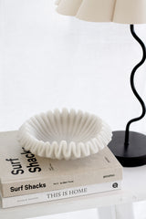 Surf Shacks Volume 2 coffee table book styled with a sculptural white dish and black wavy lamp on a neutral shelf.