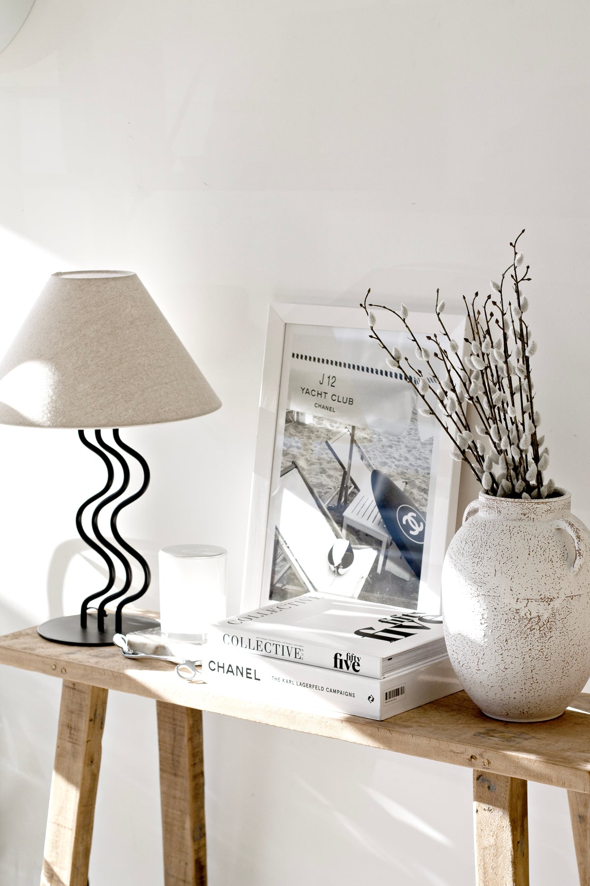 Wide view of the Surge table lamp on a console with framed art and a vase of branches