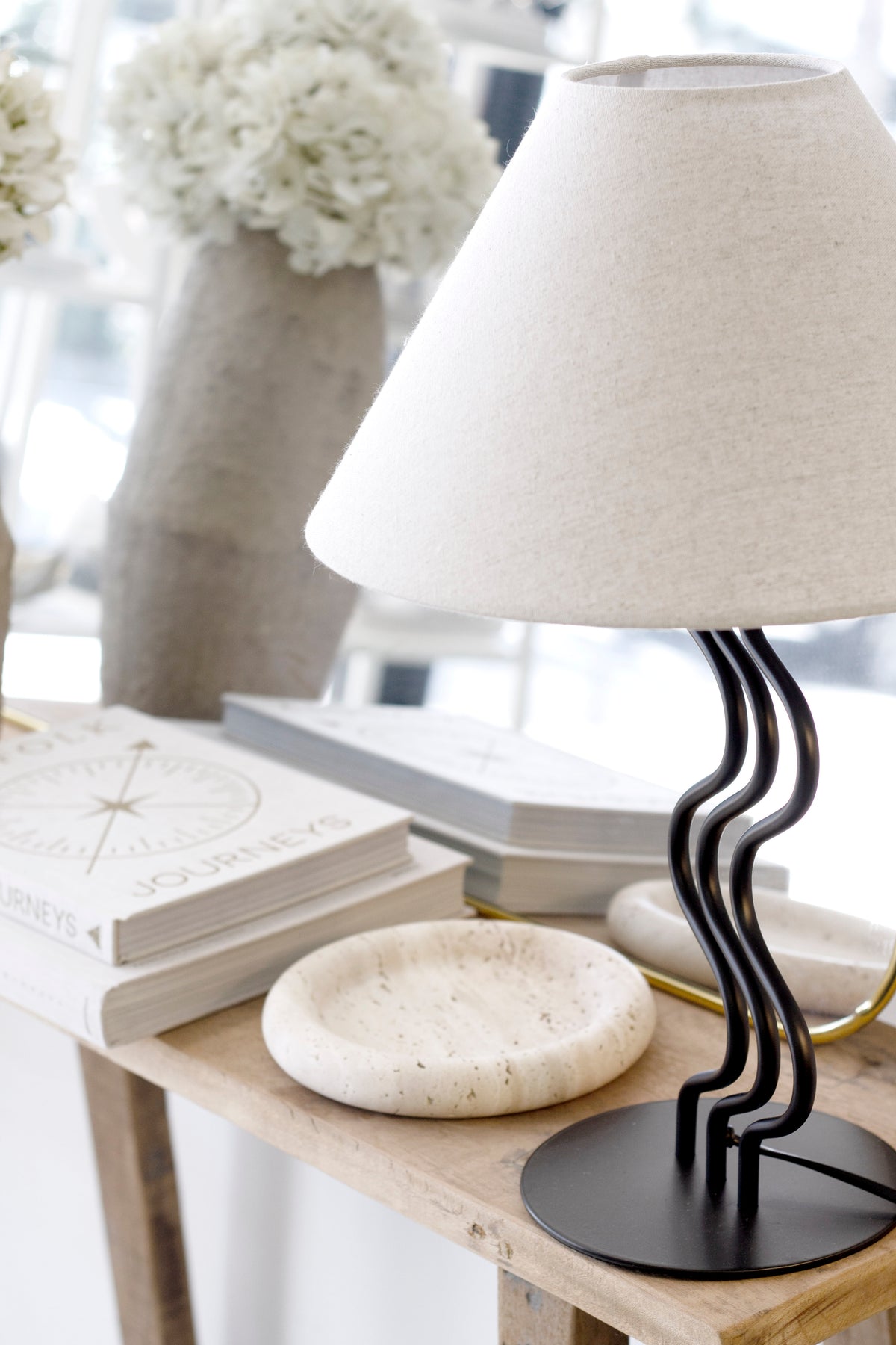 Surge table lamp on a timber console with a round travertine dish and white flowers