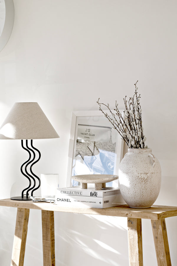 Neutral console table styled with the Surge Table Lamp, textured ceramic vase with branches, stacked books, and framed art for modern coastal styling inspiration.