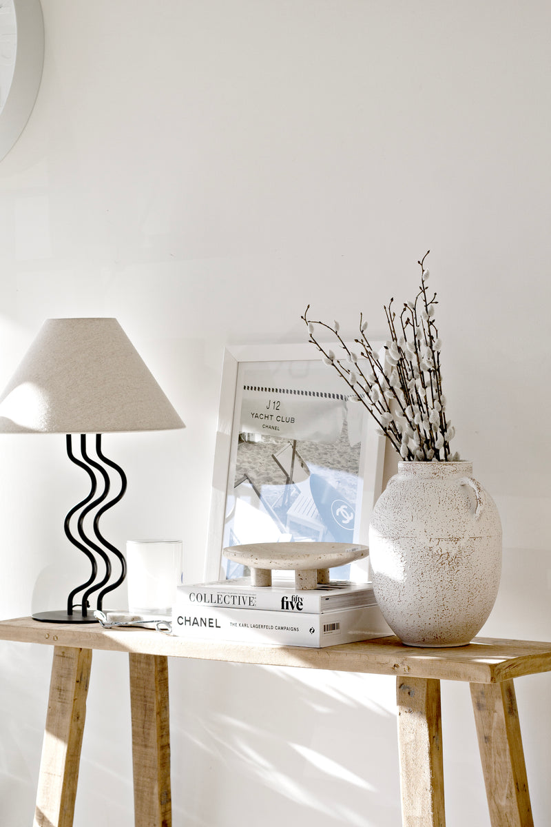 Neutral console table styled with the Surge Table Lamp, textured ceramic vase with branches, stacked books, and framed art for modern coastal styling inspiration.
