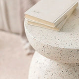 A modern Flux Home Pedestal Side Table - Fleck White with a book on top.