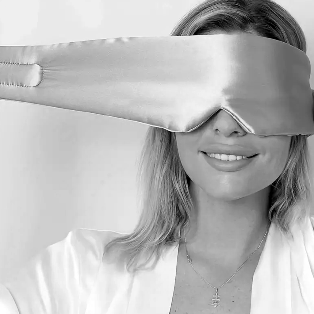 Hands holding the taupe mulberry silk eye mask up in front of a smiling face