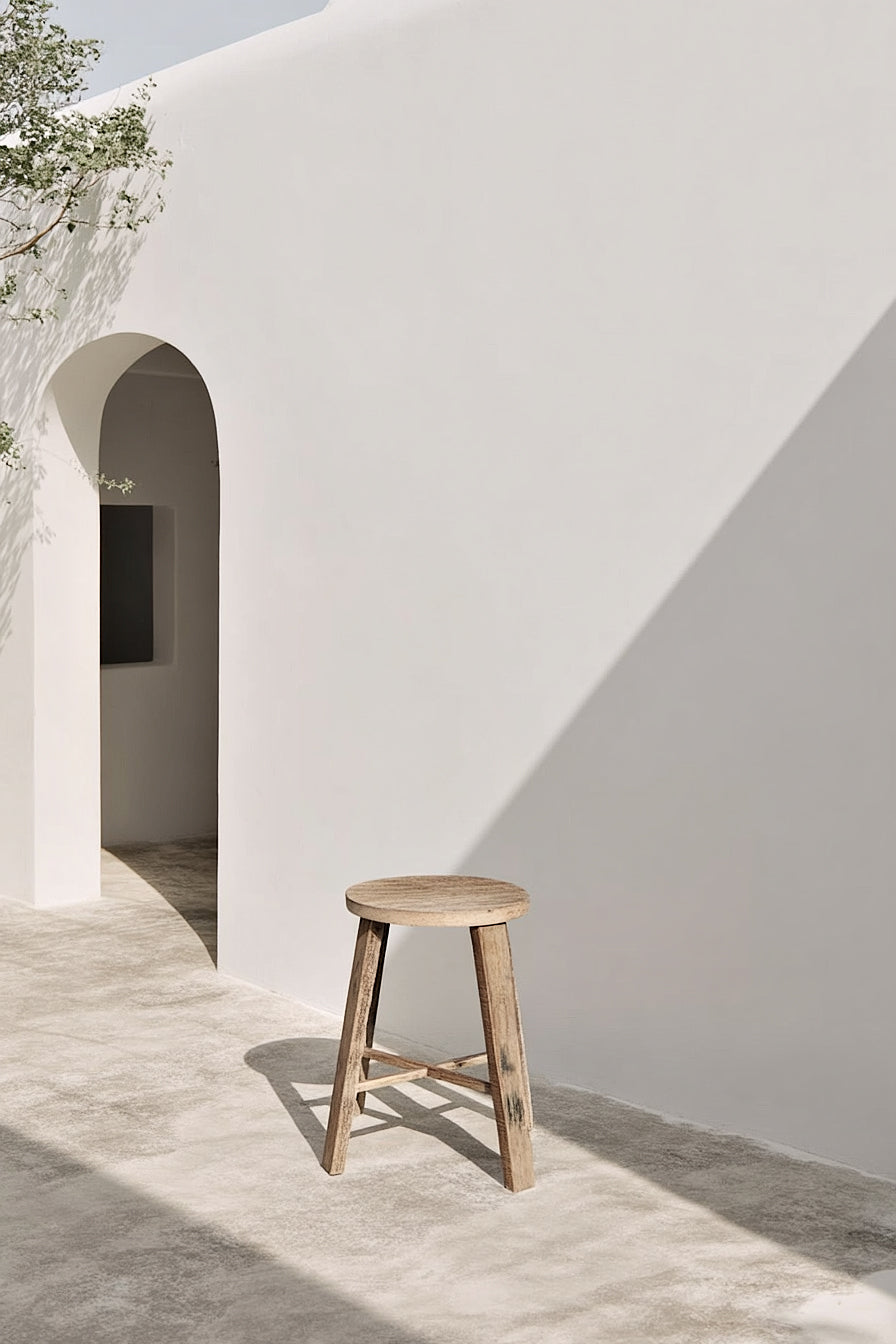 Natural teak stool outdoors against a white stucco archway