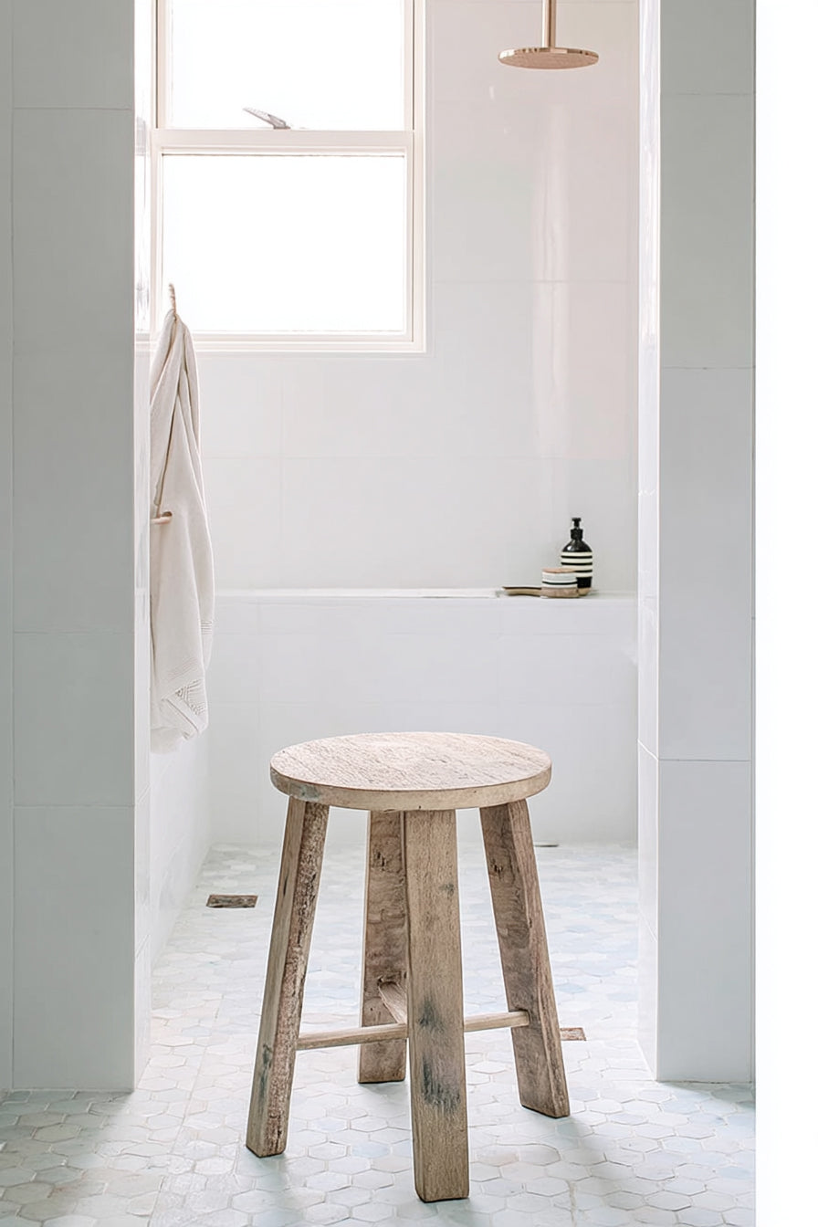 Natural teak stool on a pale bathroom floor beside a bath and a window