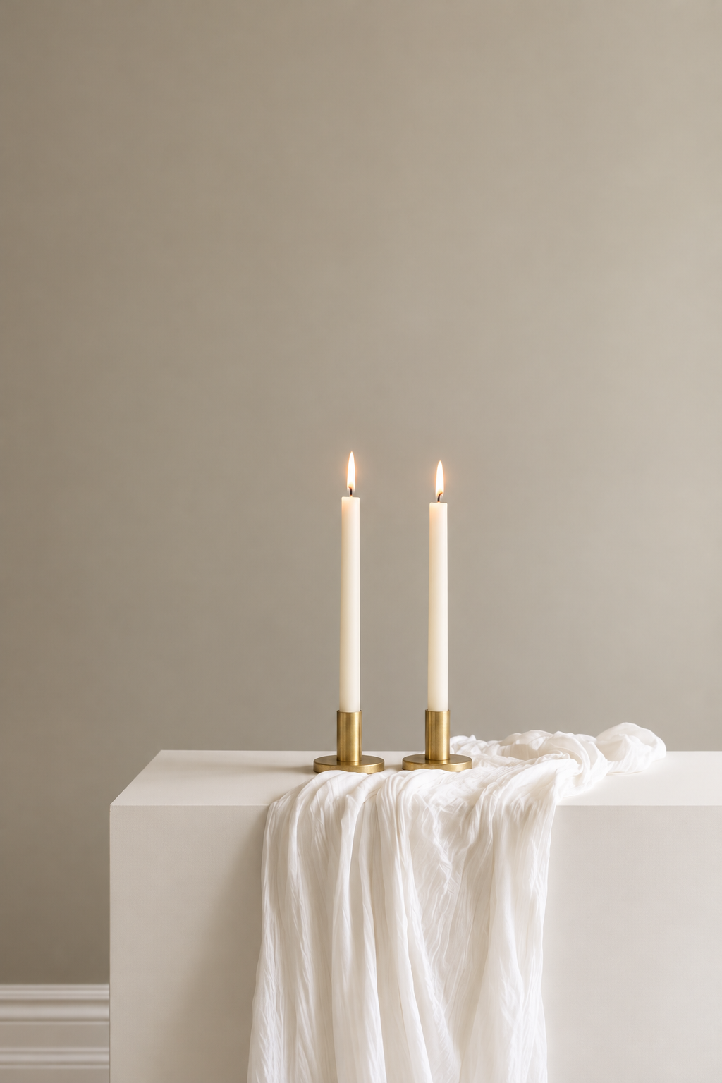 Tee Candle Sticks in solid brass with lit cream taper candles on a console with soft white linen