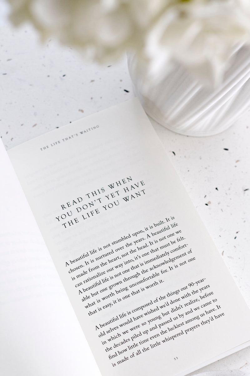 Open page of The Life That’s Waiting by Brianna Wiest, styled with soft flowers and neutral decor.