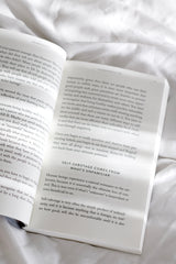 The Mountain Is You by Brianna Wiest open book on white bedding in soft neutral light