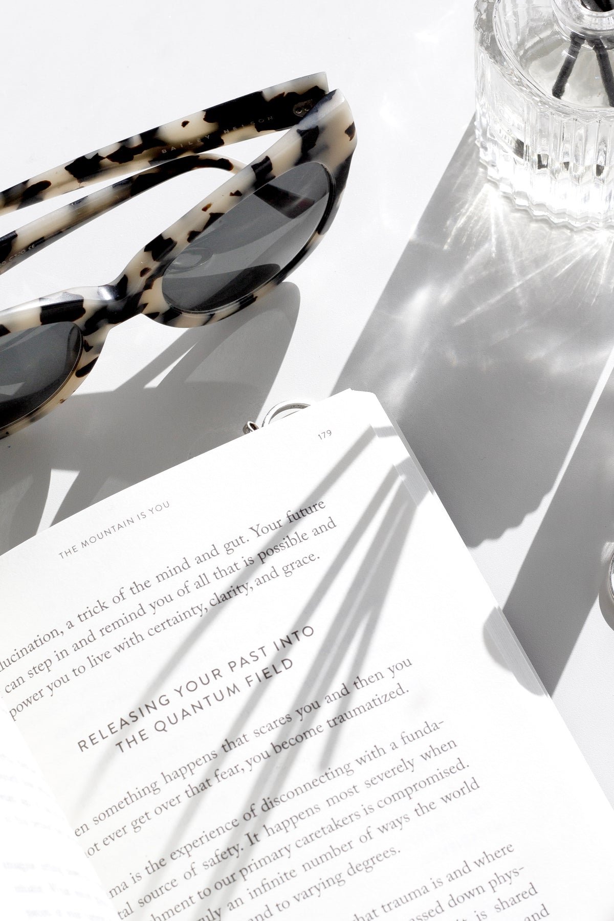 The Mountain Is You by Brianna Wiest – bestselling self-help book on overcoming self-sabotage and emotional growth - book next to Sunglasses and diffuser on white surface