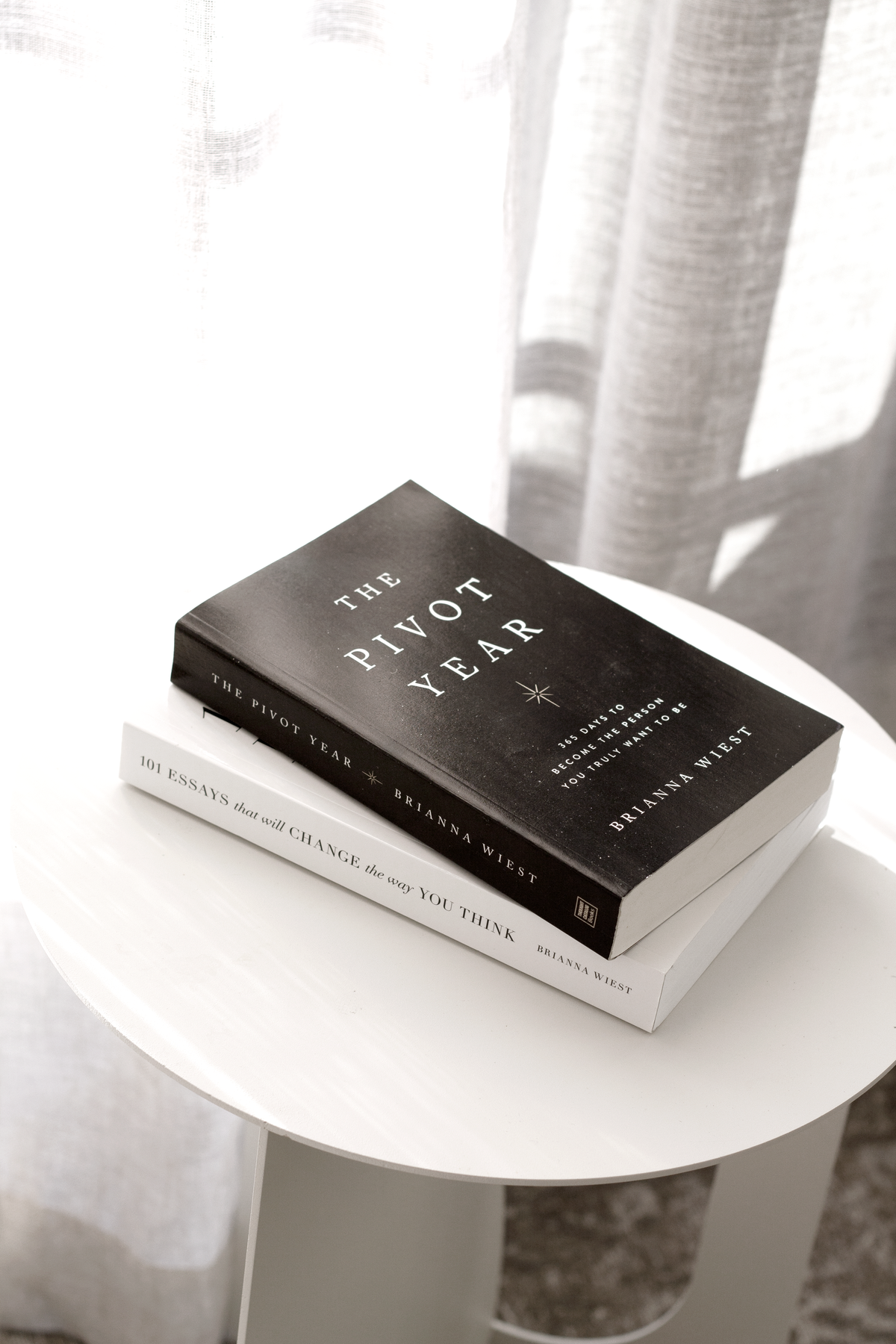 The Pivot Year hardcover resting on a paperback on a round white table by a sheer curtain