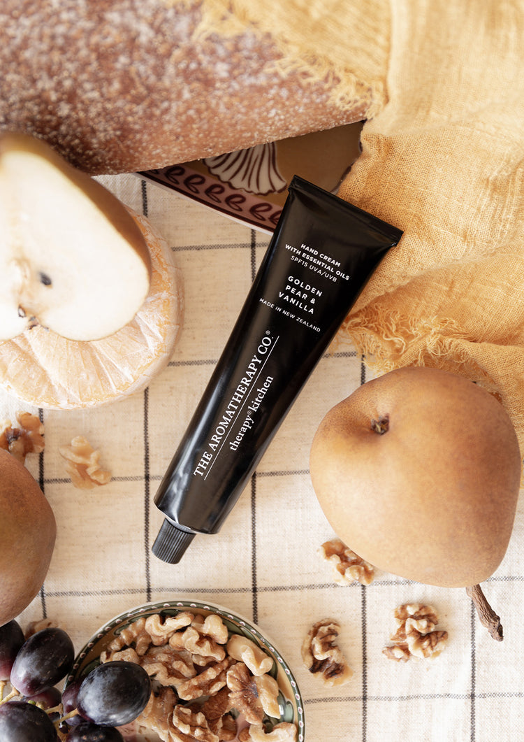 Golden Pear & Vanilla hand cream tube in a flatlay with pears, walnuts, grapes and bread on a check cloth
