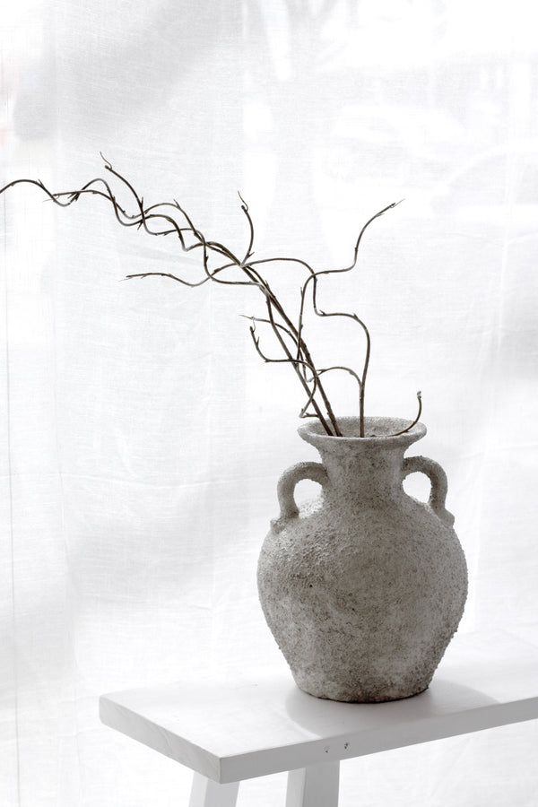 Thira Vase styled with a branch on a white plinth in soft daylight