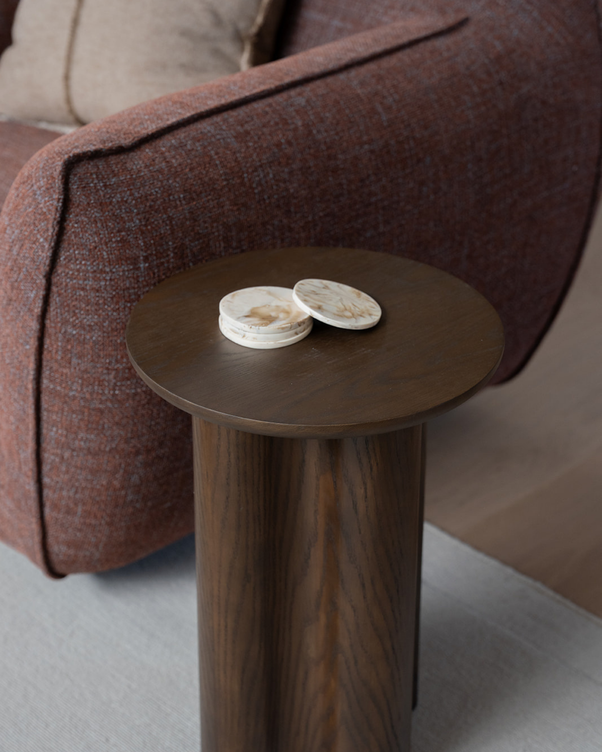 A stack of Tiramisu resin coasters on a round timber pedestal side table beside a rust armchair