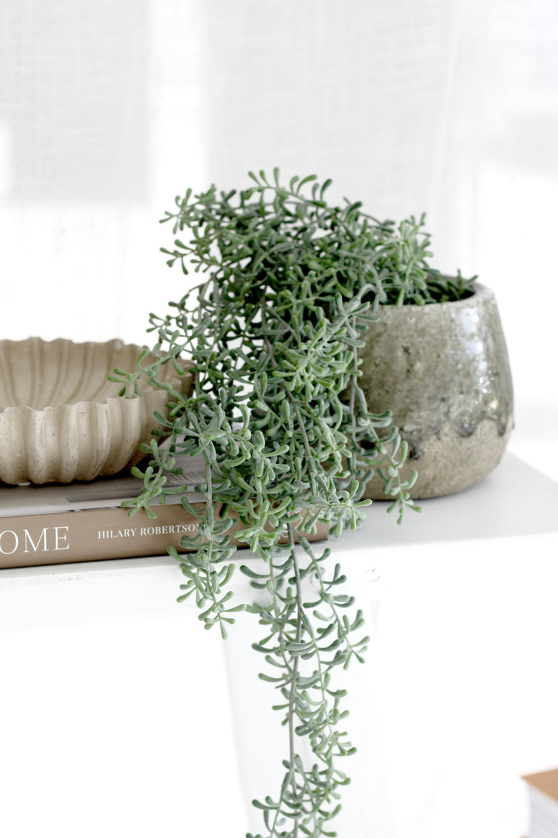 Rustic stoneware planter with cascading greenery styled on a neutral shelf.
