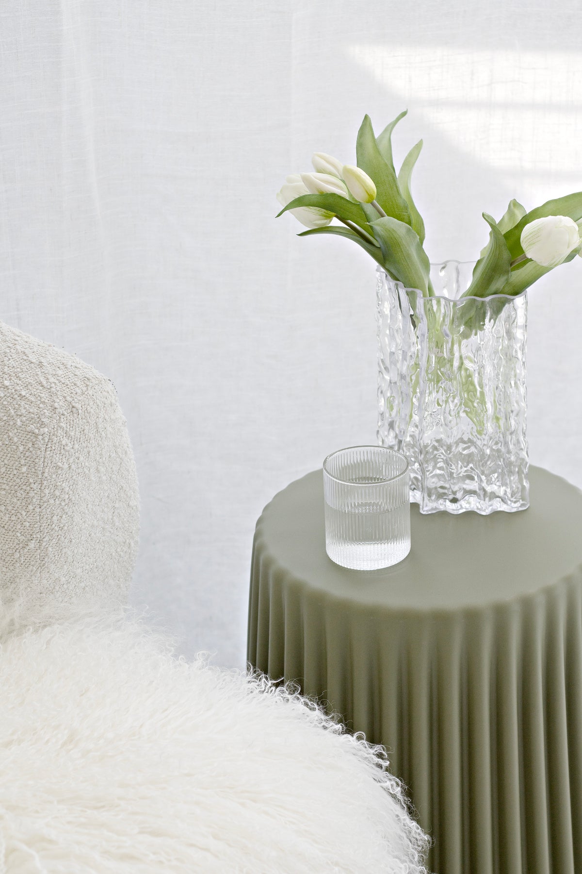 Olive ribbed stool holding a clear vase of white tulips and a ribbed tumbler beside a boucle chair